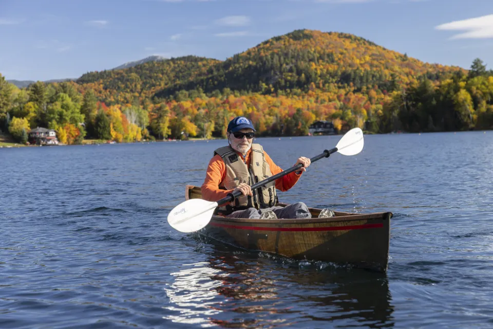 Man paddling kayak with fall colors on background mountain